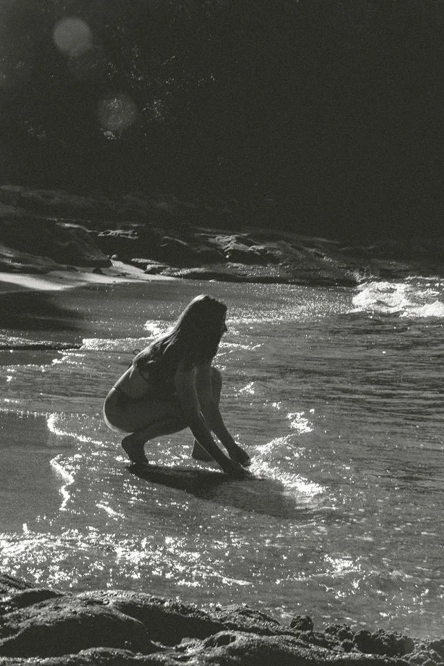 Woman crouching at the shoreline in black and white